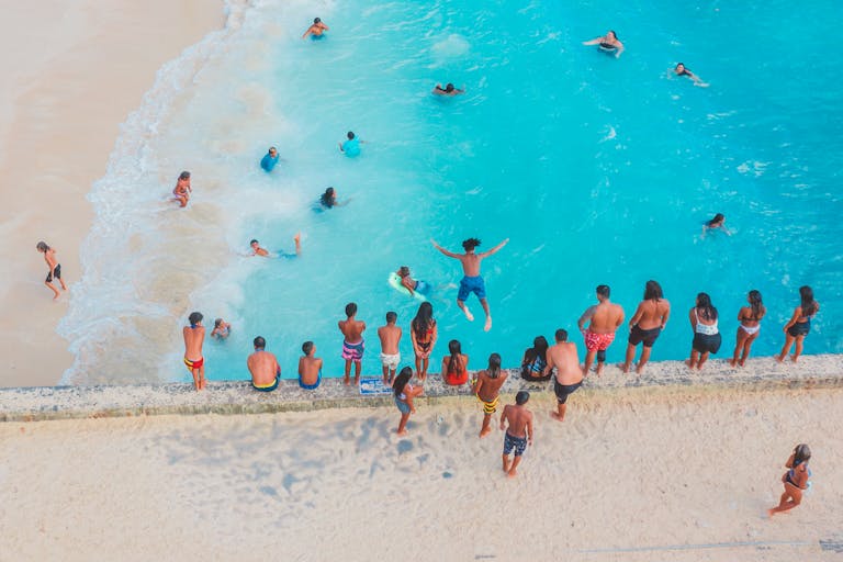 Bird's eye view of people swimming and relaxing at a tropical beach on a sunny day.